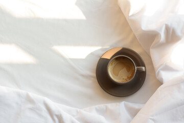 Fototapeta premium Aromatic morning coffee on bed, top view. Space for text