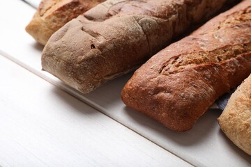 Different tasty baguettes on white wooden table, closeup