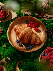 croissant on a wooden plate with berries on a forest lawn