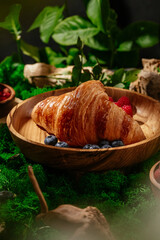 croissant on a wooden plate with berries on a forest lawn