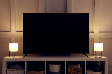 Modern TV and lamps on cabinet near white wall indoors. Interior design