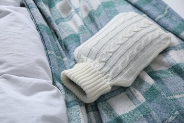 Fototapeta na wymiar Hot water bottle with knitted cover and checkered plaid on bed