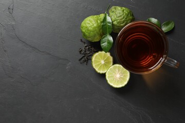 Glass cup of tasty bergamot tea, dry leaves and fresh fruits on black table, flat lay. Space for text - obrazy, fototapety, plakaty