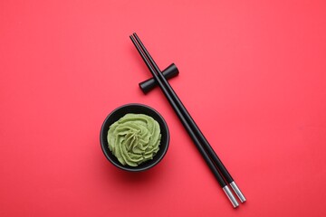 Bowl with swirl of wasabi paste and chopsticks on red background, flat lay