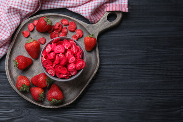 Freeze dried and fresh strawberries on black wooden table, top view. Space for text