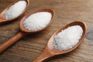 Granulated sugar in spoons on wooden table, closeup