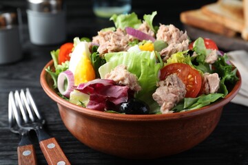 Bowl of delicious salad with canned tuna and vegetables served on black wooden table, closeup