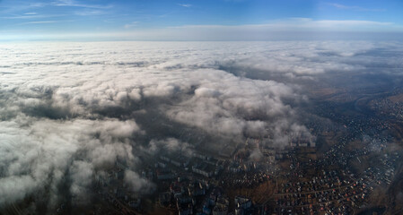 Aerial view from high altitude of distant city covered with puffy cumulus clouds forming before...