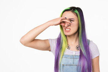Young hipster teenage girl caucasian woman with dyed colorful hair smelling stinky, closing her nose with a hand because of odor stench isolated in white background - obrazy, fototapety, plakaty