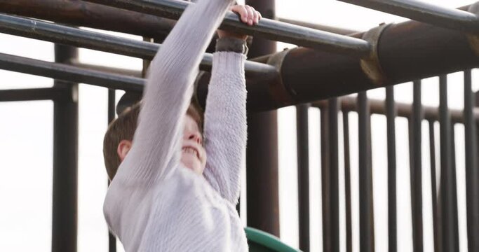 Fun and playful boy playing on monkey bars, jungle gym or playground in park, home garden or backyard. Adorable, cute and little child having fun, enjoying break and hanging or holding onto metal bar