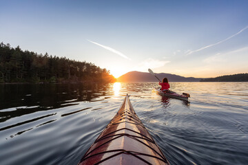 Adventurous Woman on Sea Kayak paddling in the Pacific Ocean. Sunny Summer Sunset. Taken near...