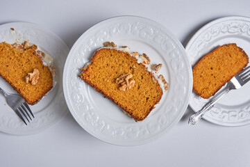Slices of homemade carrot cake with sugar glaze and walnuts served in three white dishes. Food concept