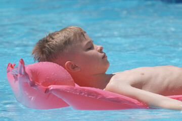 Young child boy relaxing on summer sun swimming on inflatable air mattress in swimming pool during tropical vacations. Summertime activities concept