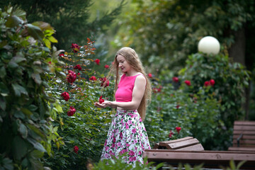 Beautiful woman with long blond hair. A woman walks in a rose garden. Beautiful rose garden. Dress with floral print.