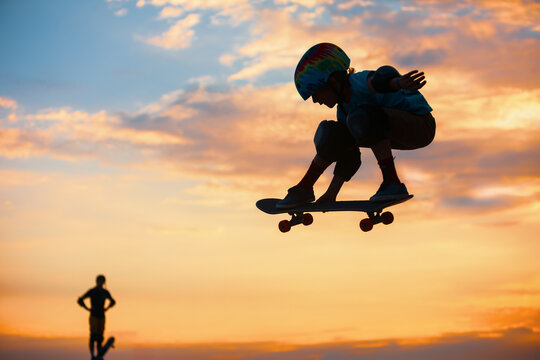 Skateboarder in action. Black silhouette of young boy making air trick with grab on skate in skatepark on sky with sun background. Street culture, skateboard riding lessons. Weekend activities.