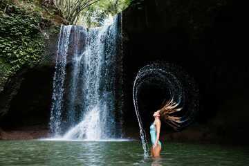 Woman have fun in natural pool under falling water of Suwat waterfall in tropical jungle. Nature...