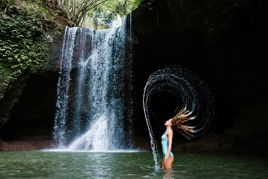 Woman have fun in natural pool under falling water of Suwat waterfall in tropical jungle. Nature day tour, hiking activity adventure and fun at family tourist camp on summer vacation in Bali island