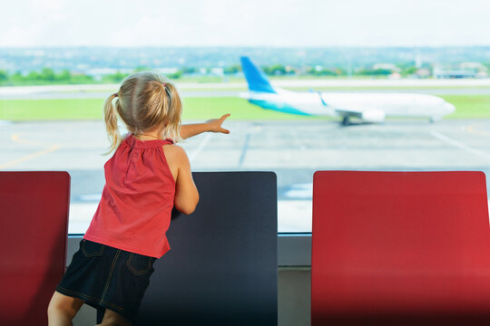 Little kid wait for boarding to plane flight in airport departure hall. Baby look through the window at flying airplane. Active family lifestyle, travel by air with children on summer vacation.