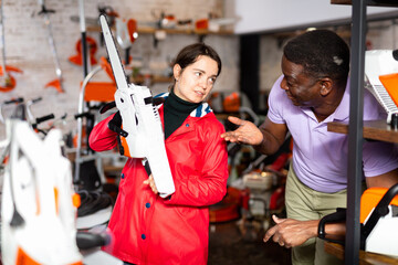 Man advises woman to choose chainsaw at a garden tool store