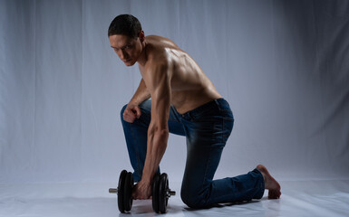 Fototapeta na wymiar Sportsman posing, with dumbbells. Photo of an active man with a naked torso on a gray background. dynamic movement. Sports and healthy lifestyle