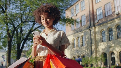 Young biracial woman booking a taxi on smartphone, holding shopping bags