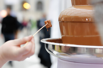 Woman holding marshmallow and frosting its in chocolate fondue fountain. Treats for the holiday...