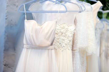 Few beautiful dresses on a hanger in wedding salon or atelier sewing studio. Wedding exhibition or...