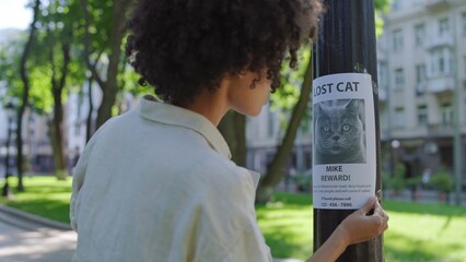 Worried woman cat owner hanging poster with lost pet picture on the tree