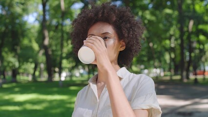 African American woman drinking her morning coffee, walking in summer park