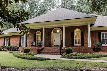 A front side view of an updated spacious red brick ranch traditional house home with off white columns and brick front steps with curb appeal - obrazy, fototapety, plakaty
