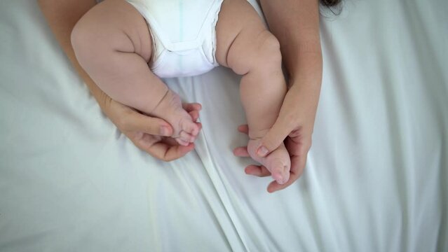 Mom hands holding newborn chubby legs. A beautiful conceptual image of motherhood and baby. Love family healthcare and medical body part. Peace calm infant toddler boy laying on soft white blanket.