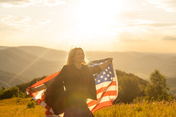 Young happy american woman with long hair holding waving on wind USA national flag on her sholders...