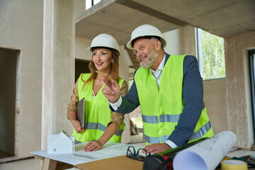 Smiling realtor and foreman inspecting house standing near table