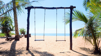 Swings on beautiful exotic beach with bright sun, sea, sand and blue sky in tropical Thailand island resort with green palm on the coast. Concept of summer vacation beach, travel and holidays.