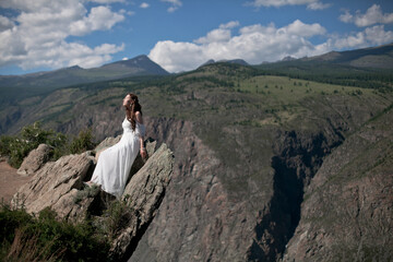 Fototapeta premium Bride in the mountains wedding image. A beautiful young woman in a wedding dress walks in the mountains.