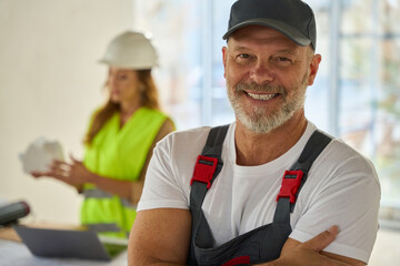 Portrait of smiling builder. Behind is realtor holding model house
