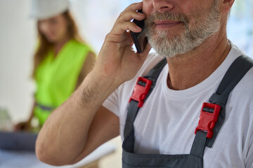Close-up face of builder with phone. Behind him stands manager