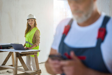 Cropped photo of builder in overalls typing message on mobile