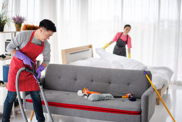 Young Asian family, Husband and wife are cleaning the house together. he is vacuuming,  using a...