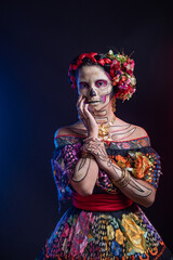 Obraz na płótnie Canvas catrina woman dressed in a mexican chiapas costume with a black background pink rebozo and skull and bones makeup on her hands