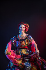 Fototapeta na wymiar catrina woman dressed in a mexican chiapas costume with a black background pink rebozo and skull and bones makeup on her hands