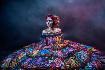 Catrina-Frau in einem mexikanischen Chiapas-Kostüm mit schwarzem Hintergrund, rosa Rebozo und Totenkopf-Make-up an den Händen