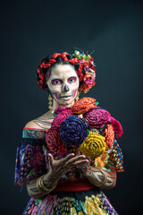 catrina woman dressed in a mexican chiapas costume with a black background pink rebozo and skull and bones makeup on her hands