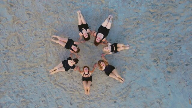 Yoga at ocean beach, group of mixed-age women sitting at circle practicing and meditating at sunset. Healthy active lifestyle and outdoor training concepts