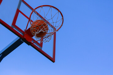 A basketball in a net on a blue sky background. The ball hit the ring. 