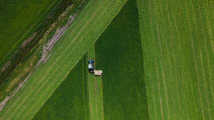 Aerial view of farming tractor mowing green field.