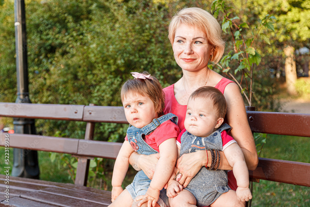 Wall mural beautiful mother with her daughter and son are sitting on a bench in the park in the summer