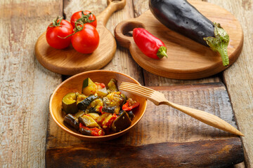 A plate of grilled vegetables next to tomatoes and eggplant on wooden boards.