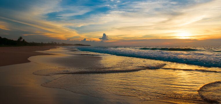 Beautiful sunset over the beach by the tropical sea. Wide photo.