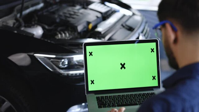 Car service mechanic uses laptop computer with green screen mock up chroma key car diagnostic software. Interactive diagnostics software on an advanced computer. Automotive electronic diagnostic app